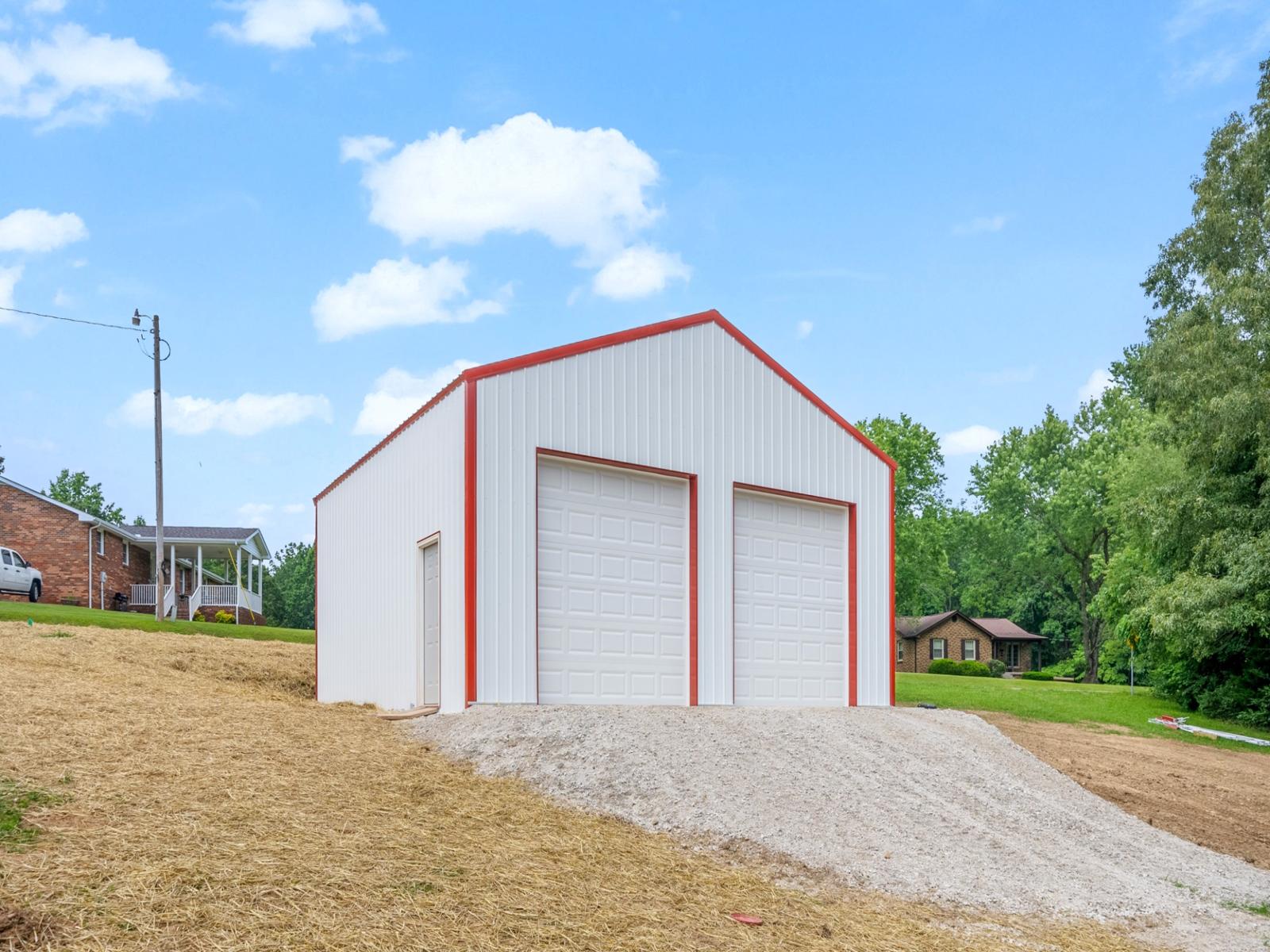 Custom-built white metal pole barn garage with red trim and dual overhead doors, measuring thirty by thirty feet with twelve-foot walls, constructed on a four-inch concrete pad—perfect for post frame buildings, residential storage, workshops, or vehicle parking.