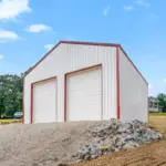 Custom-built white metal pole barn garage with red trim and dual overhead doors, measuring thirty by thirty feet with twelve-foot walls, constructed on a four-inch concrete pad—perfect for post frame buildings, residential storage, workshops, or vehicle parking.