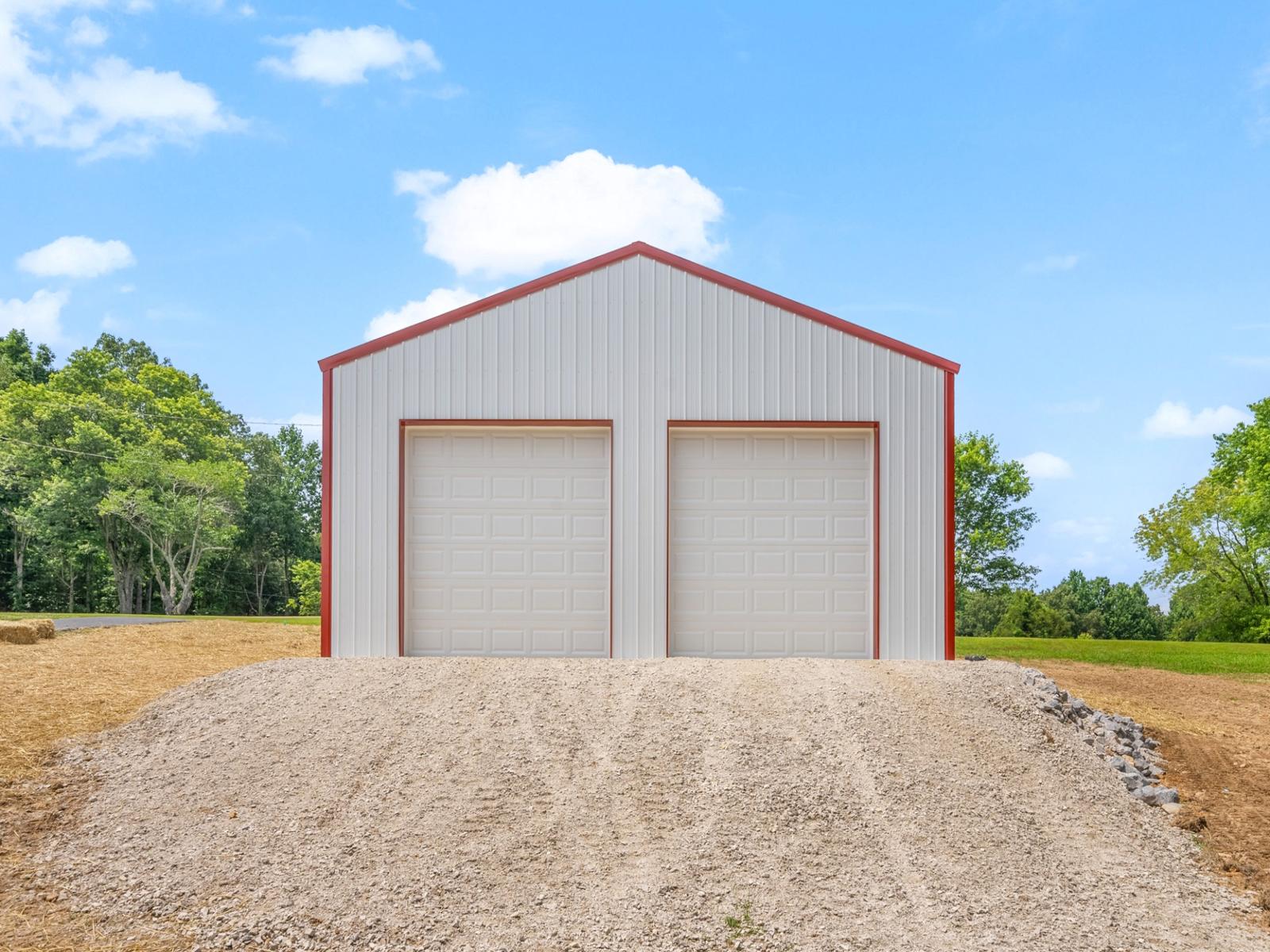 Custom-built white metal pole barn garage with red trim and dual overhead doors, measuring thirty by thirty feet with twelve-foot walls, constructed on a four-inch concrete pad—perfect for post frame buildings, residential storage, workshops, or vehicle parking.